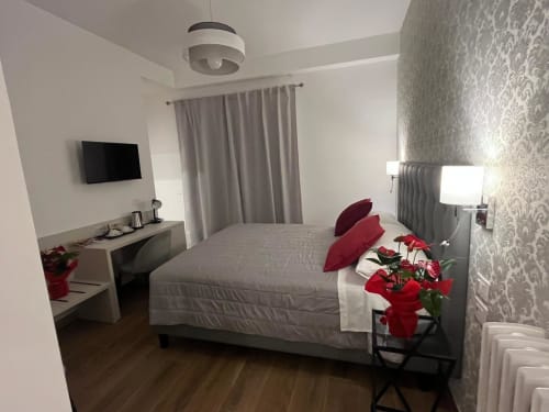 Camera moderna a Maritza Guest House Roma con letto grigio, cuscini rossi, TV a parete e vista sulla città