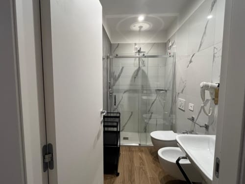 Bagno moderno della Maritza Guest House Roma con doccia, doppio lavabo, piastrelle in marmo e pavimento in legno