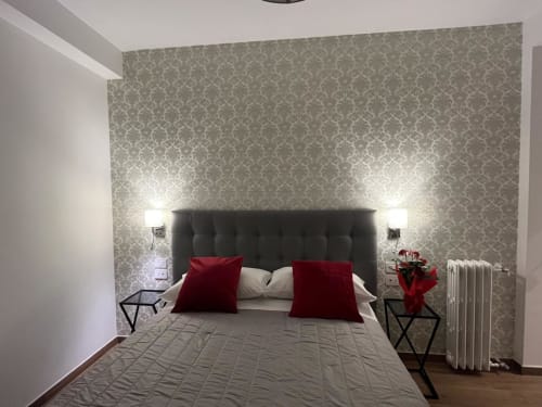 Camera da letto della Maritza Guest House Roma con carta da parati decorata, testata nera, cuscini rossi e vista sulla città