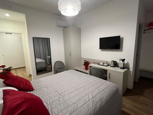 Camera moderna a Maritza Guest House Roma con letto matrimoniale, cuscini rossi, TV a parete e angolo cottura