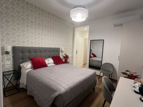 Camera moderna alla Maritza Guest House Roma con letto grigio imbottito, cuscini rossi, carta da parati decorativa e vista sulla città