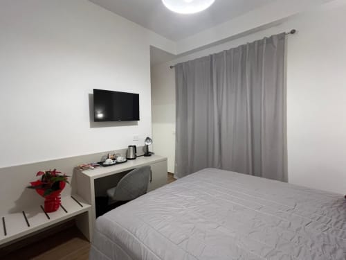 Camera moderna di Maritza Guest House Roma con letto bianco, scrivania, TV, tende grigie e fiori rossi
