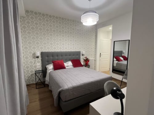 Camera moderna presso Maritza Guest House a Roma con letto imbottito grigio, cuscini rossi, carta da parati decorata e vista sulla città