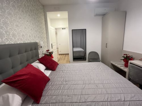Camera moderna a Maritza Guest House Roma con letto trapuntato grigio, cuscini rossi e vista sulla città