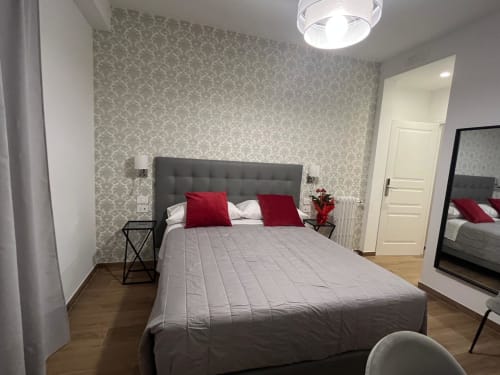 Camera moderna della Maritza Guest House Roma con letto imbottito grigio, cuscini rossi, carta da parati decorativa e pavimenti in legno