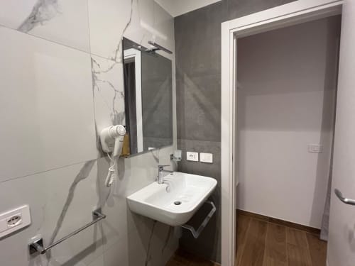 Bagno moderno della Maritza Guest House Roma con lavabo bianco, specchio, rivestimenti in piastrelle scure e ingresso alla doccia