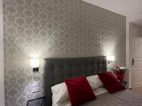 Camera della Maritza Guest House Roma con carta da parati a damasco grigio, testata scura, cuscini rossi e applique murali