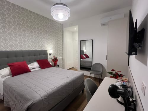 Camera moderna alla Maritza Guest House Roma con letto grigio, cuscini rossi, carta da parati decorativa e vista sulla città