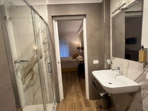 Bagno moderno della Maritza Guest House Roma con doccia in marmo, lavabo bianco e pavimento effetto legno