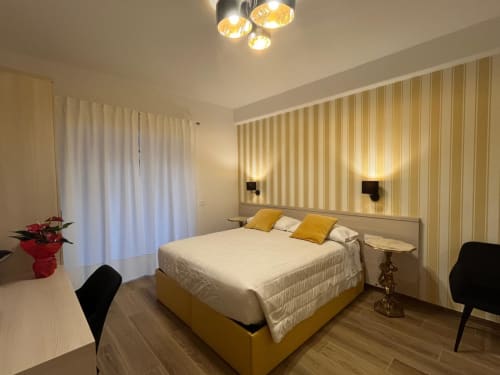 Camera moderna nella Maritza Guest House Roma con letto giallo, carta da parati a righe, luci a sospensione e vista sulla città