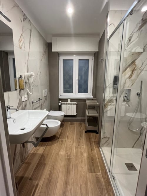 Bagno moderno della Maritza Guest House Roma con pareti in marmo, pavimento in legno, lavabo, wc e doccia walk-in
