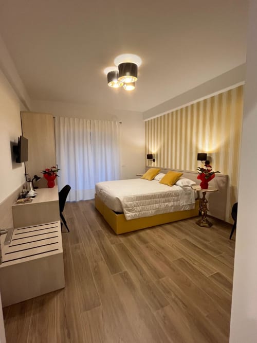 Camera moderna della Maritza Guest House Roma con letto giallo, tende rigate, pavimento in legno e vista sulla città