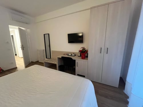 Camera moderna alla Maritza Guest House di Roma con letto bianco, scrivania, TV, armadio e pavimenti in legno