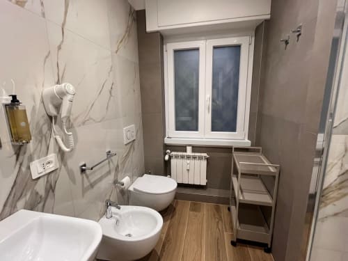 Bagno moderno presso la Maritza Guest House Roma con rivestimenti in marmo, bidet, wc e finestra con vista sulla città.