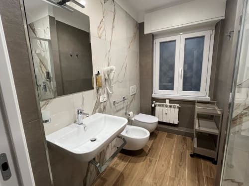 Bagno moderno a Maritza Guest House Roma con pareti in marmo, lavandino bianco, bidet e pavimento effetto legno