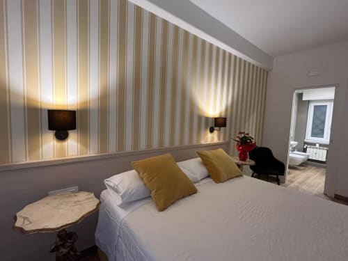 Camera moderna alla Maritza Guest House Roma con letto bianco, cuscini dorati, parete a righe, applique e vista sulla città