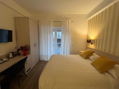Camera moderna della Maritza Guest House a Roma con letto matrimoniale, cuscini gialli, scrivania, vista balcone e illuminazione calda
