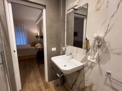 Bagno moderno della Maritza Guest House Roma con lavabo bianco, piastrelle in marmo e vista verso la camera da letto