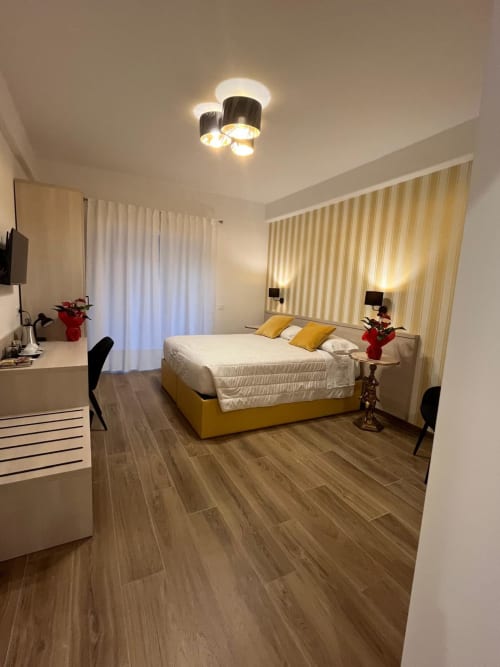 Camera moderna alla Maritza Guest House Roma con letto giallo, tende a righe, pavimenti in legno e illuminazione soffusa