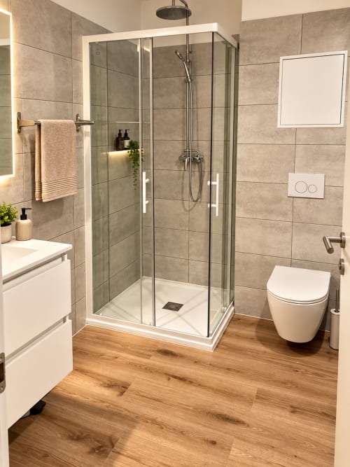 Salle de bain moderne de la villa ALMA ROSSA à Lecci avec douche vitrée, sanitaires blancs et revêtement imitation bois
