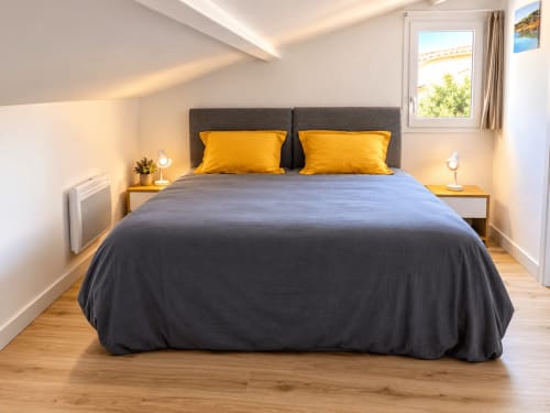 Chambre moderne de la villa ALMA ROSSA à Lecci, avec lit gris, coussins jaunes, tables de nuit en bois et vue sur la piscine