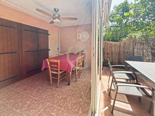 Salle à manger avec nappe rose et chaises en bois ouvrant sur la terrasse, ventilateur de plafond, carrelage rouge, vue sur le jardin de la villa de Calvi