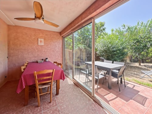 Salle à manger avec nappe à pois rouges et chaises en bois, ouverte sur un patio-jardin meublé et verdoyant