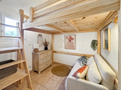 Chambre de villa lumineuse avec poutres en bois, lit mezzanine, canapé blanc et décoration naturelle près de la plage de Calvi