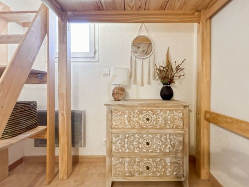 Entrée lumineuse de la villa Calvi avec escalier en bois, dresser sculpté, miroir décoratif, lampe et fleurs séchées