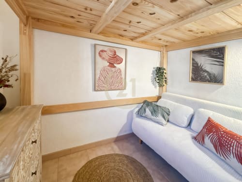 Chambre lumineuse de villa à Calvi avec poutres en bois, lit blanc, coussins décoratifs, art botanique encadré et lumière naturelle