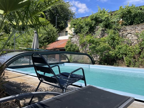 Piscine extérieure avec couverture rétractable du gîte Le Petit Moulin à Pouzauges, entourée de murs en pierre et de verdure luxuriante
