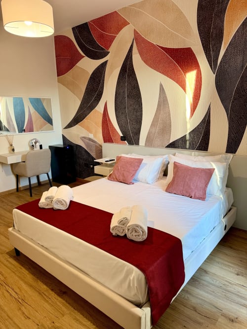 Camera deluxe Hotel Il Mulino con carta da parati a motivi vegetali, letto bianco, passatoia rossa e zona lavoro