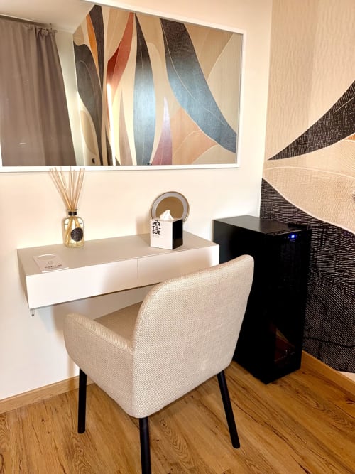 Elegante area reception di IL MULINO con poltrona color crema, scrivania bianca con cassetti, diffusore di fragranza e arte astratta murale a Casalgrande