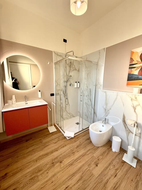 Bagno moderno dell'Hotel Il Mulino con vanity rosso, specchio circolare, doccia in marmo e pavimento in legno