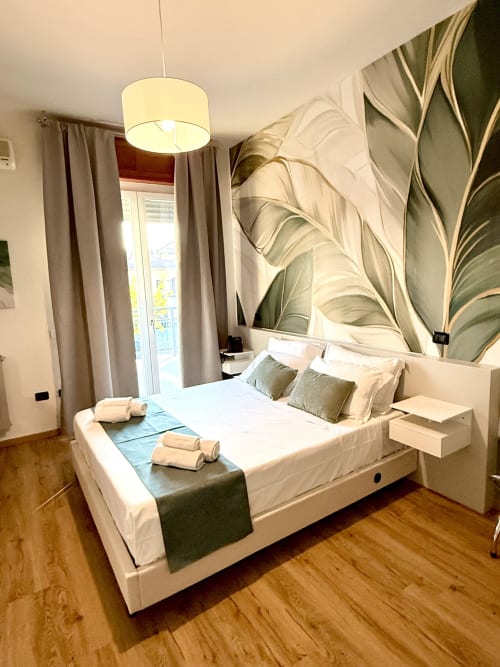 Camera lusso dell'Hotel Il Mulino con letto matrimoniale, murale botanico, lampada a sospensione e accesso al balcone
