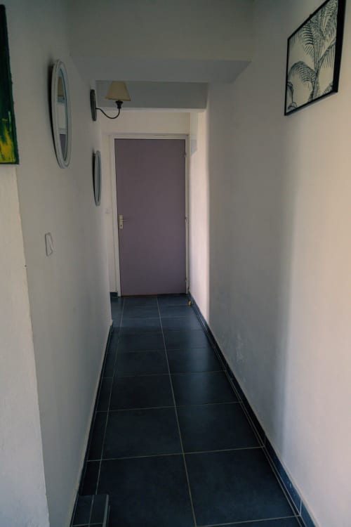 Couloir étroit au sol carrelé noir, murs blancs et porte violette du gîte Le Nid De Bellemont à Trois-Rivières