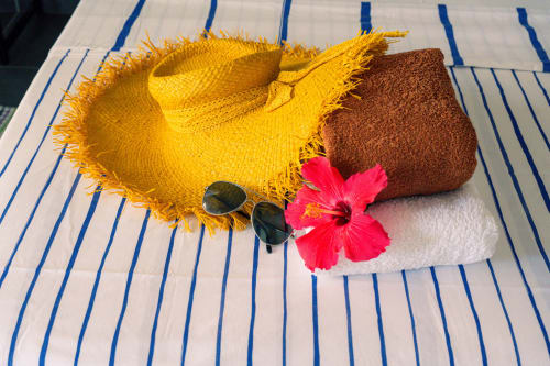 Essentiels de vacances à la plage sur serviette rayée : chapeau de paille jaune, lunettes de soleil, fleur d'hibiscus rose et portefeuille marron
