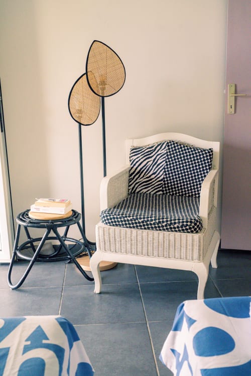 Coin salon cosy au Nid De Bellemont avec fauteuil en rotin blanc, coussins patterné, lampadaire décoratif et