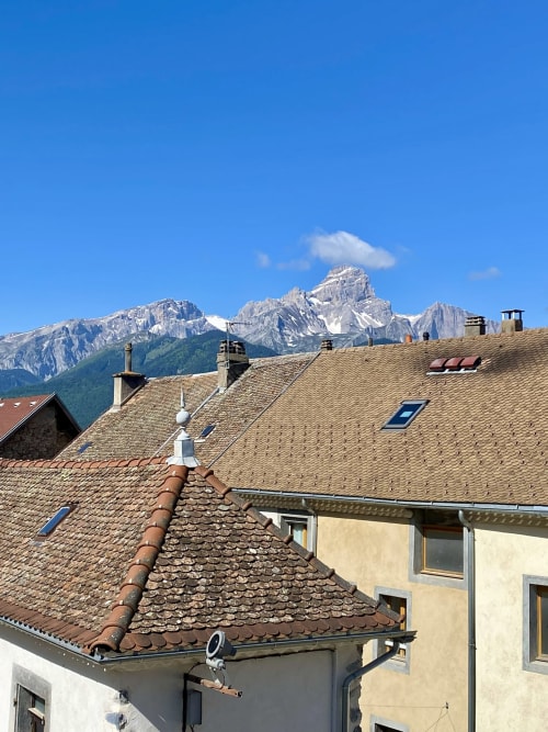 Toits de l'Hôtel le Tilleul avec les pics alpins en arrière-plan à Corps, France, sous un ciel bleu dégagé