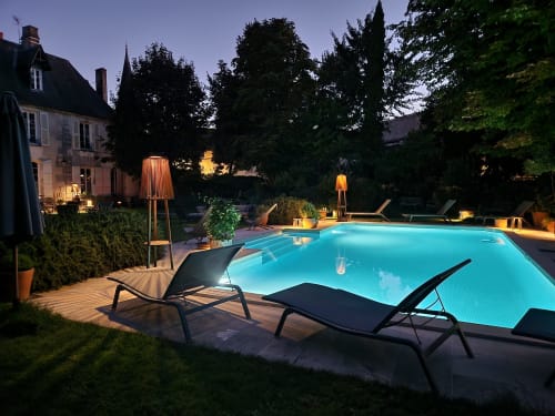 Piscine du Logis des Tourelles à la tombée du jour, Cognac. Bassin illuminé avec transats, terrasse éclairée et manoir.