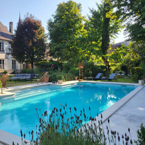 Piscine du Logis des Tourelles à Cognac avec chaises longues, pelouse impeccable, arbres et bâtiments historiques