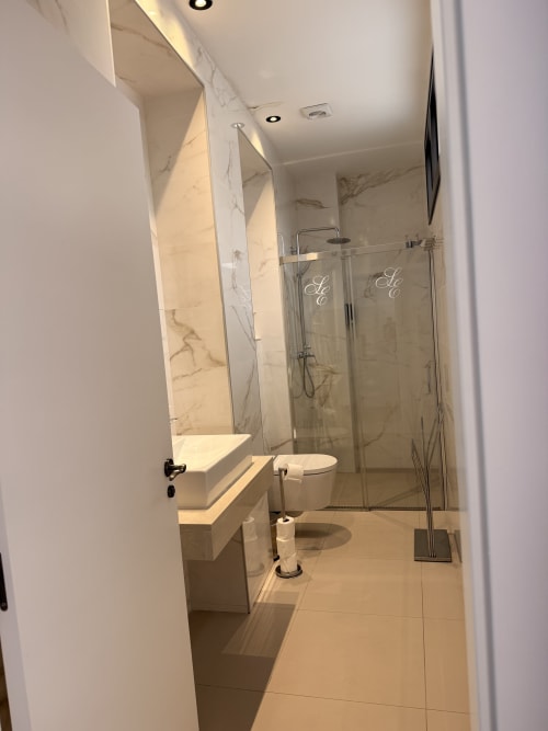 Baño moderno en la Suite Giraldillo del Edificio San Esteban 16, Sevilla, con paredes de mármol, ducha de cristal, inodoro y
