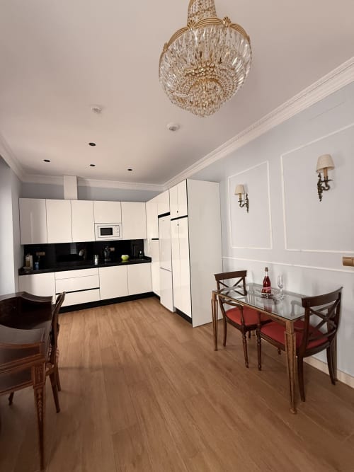 Cocina y comedor de la Suite Giraldillo en Sevilla con muebles blancos, encimera negra, mesa de madera y sillas rojas