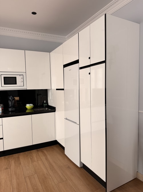 Cocina moderna en apartamento de Sevilla con muebles color crema, encimera negra, microondas y refrigerador alto con marco negro