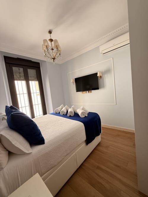 Dormitorio moderno en Edificio San Esteban 16 de Sevilla con cama blanca, detalles azules, TV de pantalla plana y puertas
