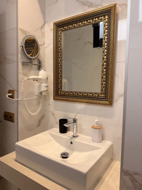 Lujoso baño de la Suite Giraldillo de Sevilla con espejo dorado ornamentado, lavabo blanco de cristal y paredes de mármol