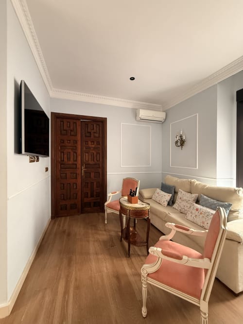 Sala de estar de la Suite Giraldillo en Sevilla con sofá beige, sillas color coral, puertas de madera oscura y televisor de pantalla plana