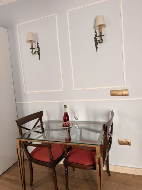 Elegante comedor en la Suite Giraldillo, Sevilla con mesa de vidrio, sillas tapizadas en rojo y apliques decorativos en la pared