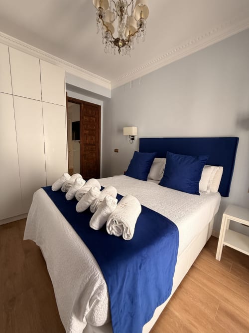 Dormitorio moderno en Edificio San Esteban 16, Sevilla, con cabecero azul marino, ropa de cama blanca, toallas enrolladas y cristalería