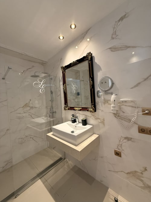 Lujoso baño de mármol en la suite del Edificio San Esteban 16 de Sevilla con espejo ornamental, lavabo sobre encimera, ducha a ras de suelo y